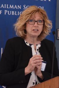 A woman with blond hair and glasses speaks at a podium in front of a Columbia backdrop